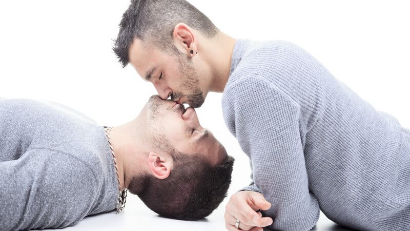 Schwules Paar in grauen Pullovern küsst sich auf dem Boden vor weißem Hintergrund