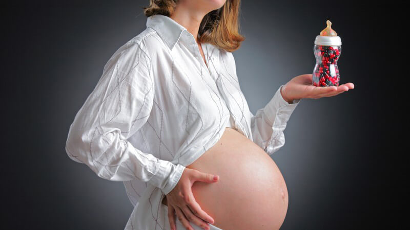 Schwangere Frau mit dickem Babybauch in weißer Kleidung vor einem schwarzen Hintergrund