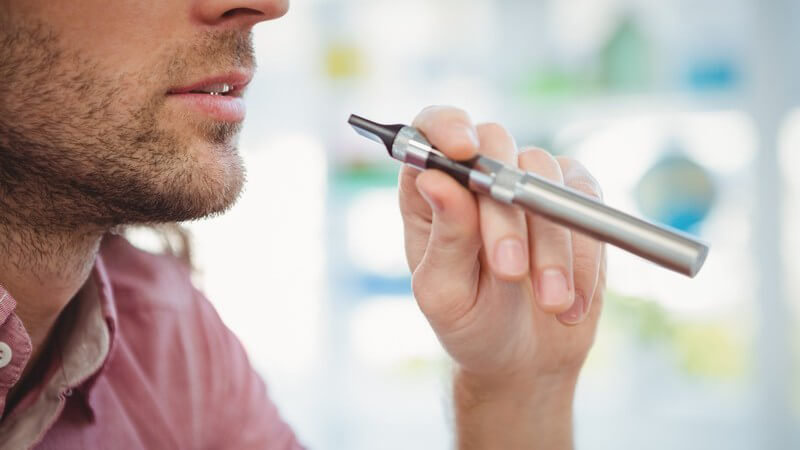 Mann mit Dreitagebart hält eine silberne E-Zigarette