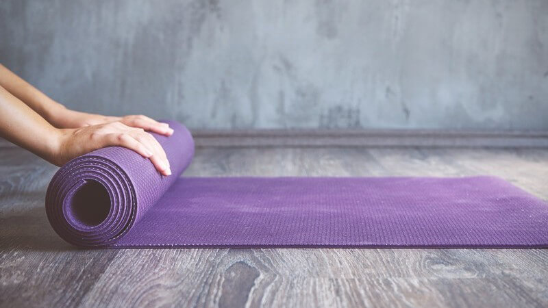Frau rollt eine lilafarbene Yogamatte zusammen