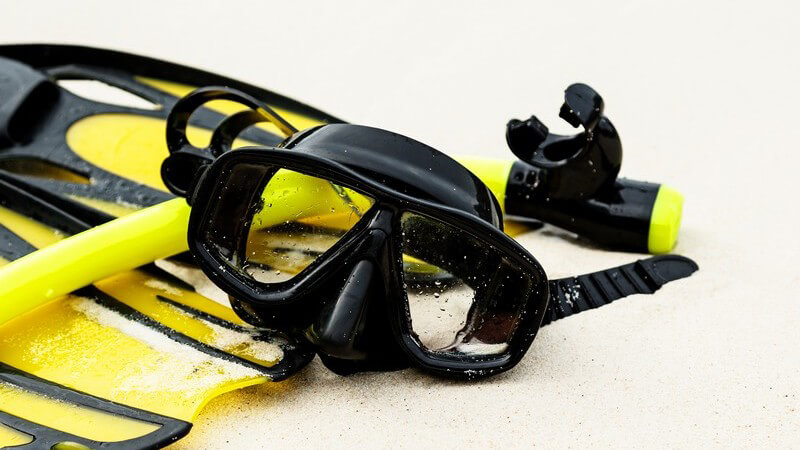 Schwarz-gelbe Schnorchelausrüstung mit Maske, Schnorchel und Flossen im feinen Sand