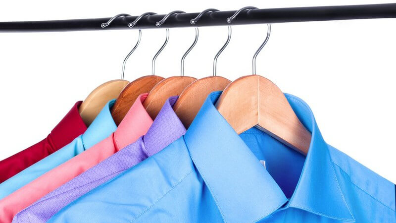Fünf farbige Hemden hängen auf Bügeln an einer Kleiderstange