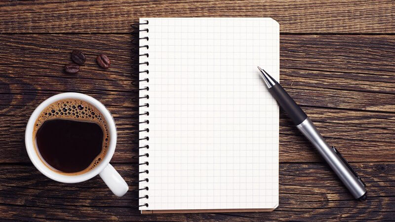Kleiner Notizblock mit Kugelschreiber und Tasse Kaffee auf einem dunklen Holztisch