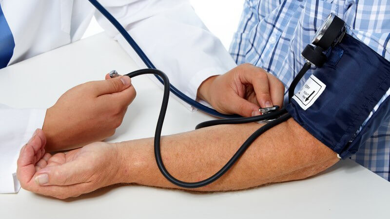 Arzt misst den Blutdruck am linken Arm eines Patienten in blauem Karohemd