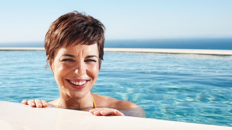 Junge Frau im Pool am Beckenrand lächelt in Kamera