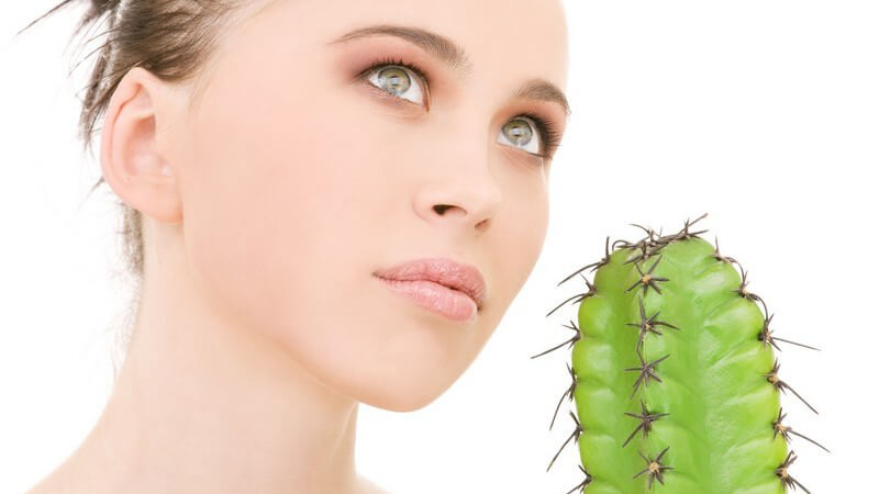 Junge Frau vor Kaktus schaut nach oben, weißer Hintergrund