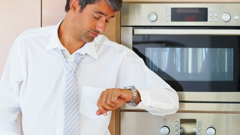 Mann in Küche schaut ungeduldig auf Armbanduhr