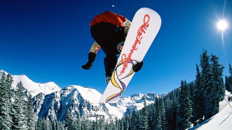 Snowboarder in der Luft vor blauem Himmel in Schneelandschaft