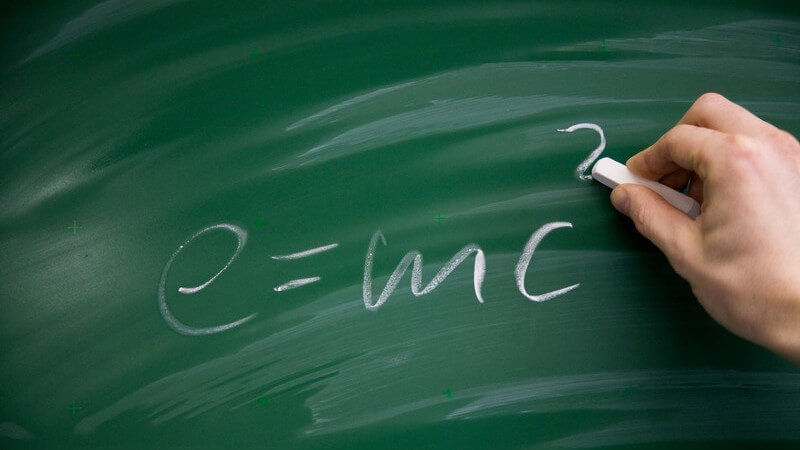 Rechte Hand eines Lehrers schreibt mit Kreide Relativitätstheorie bzw. Formel an Tafel
