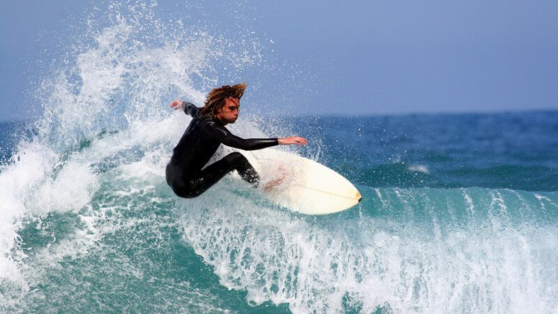 Mann in Neoprenanzug auf weißem Surfbord in einer blauen Welle