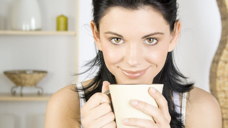 Junge lächelnde Frau hält Becher mit Tee in Händen