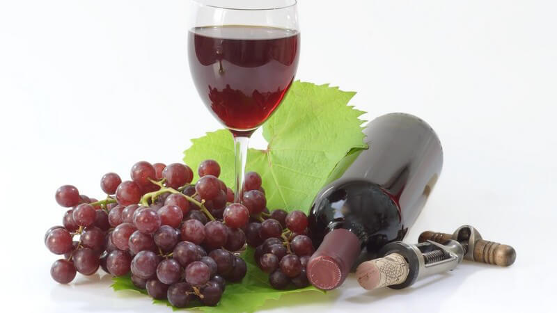 Glas mit Rotwein, dunkle Weintraube, liegende Flasche Rotwein und Korkenzieher