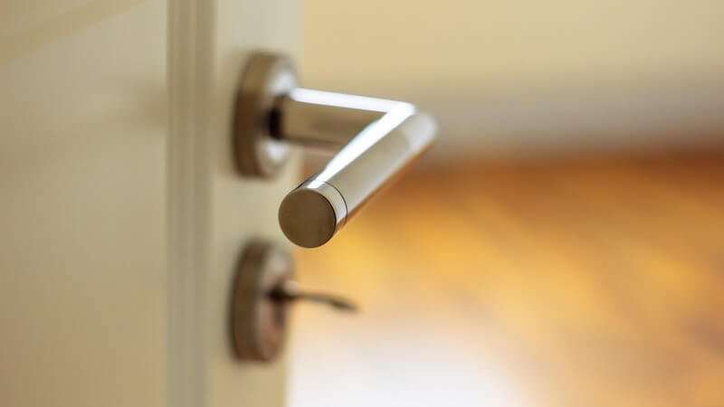 Weiße, leicht geöffnete Zimmertür mit Klinke und Schlüssel im Schlüsselloch