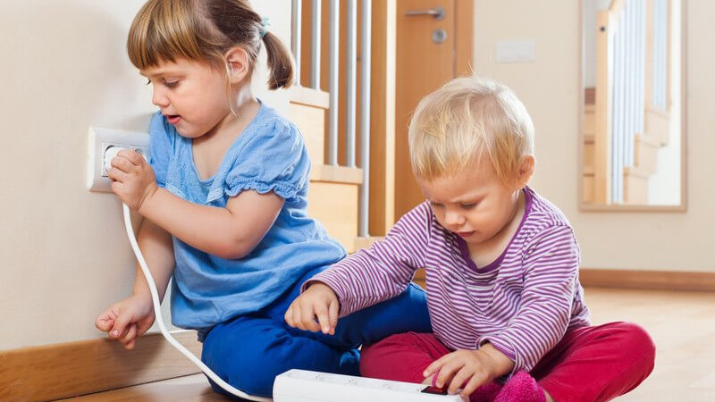 Zwei Kleinkinder spielen mit einer Mehrfachsteckdose an einer Steckdose herum