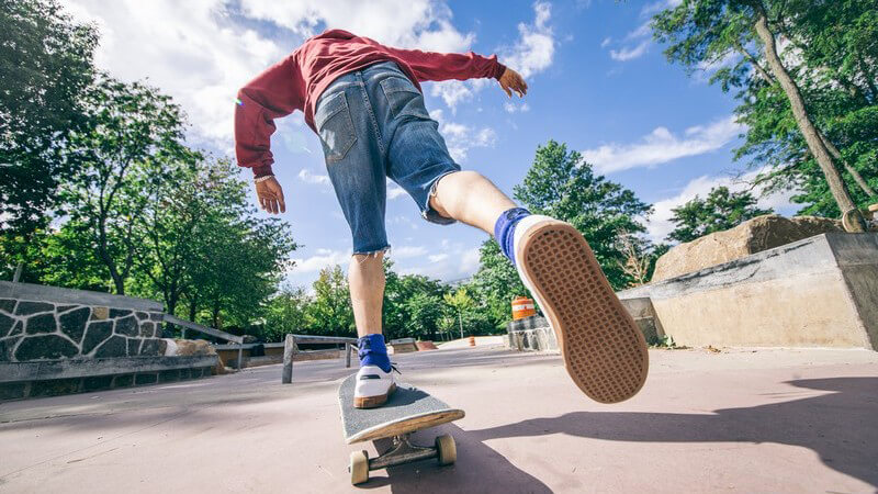 Junge in abgeschnittener Jeanshose fährt Skateboard in einem Park