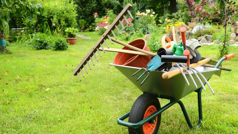 Gartenarbeit - Schubkarre mit Harken, Blumentöpfen, Gießkanne, Schaufel und Handschuhen