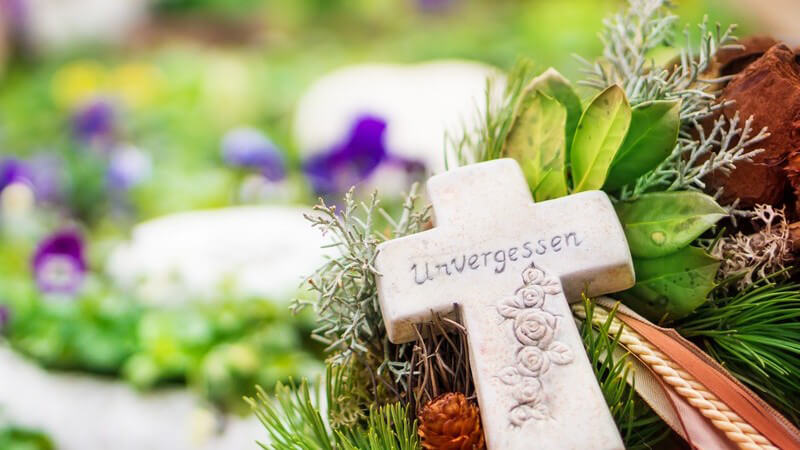 Nahaufhnahme Grabschmuck auf Friedhof mit Kreuz, auf dem "Unvergessen" geschrieben steht