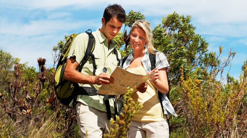 Junges Paar in Natur mit Rucksäcken schaut auf Karte