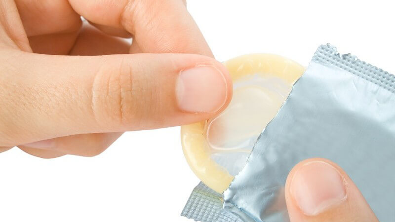 Hand nimmt helles Kondom aus silberner Verpackung