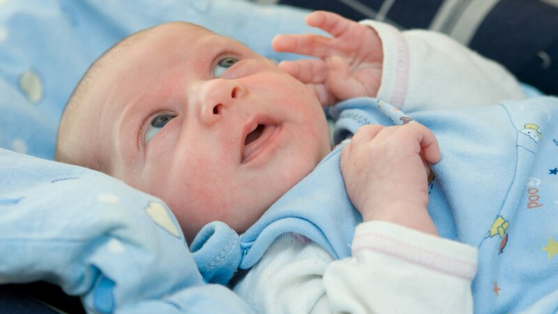 Neugeborenes in blauer Kleidung schaut neugierig nach oben
