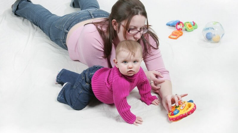Mutter und Kind mit rosa Pullover spielen mit Greifspielzeug