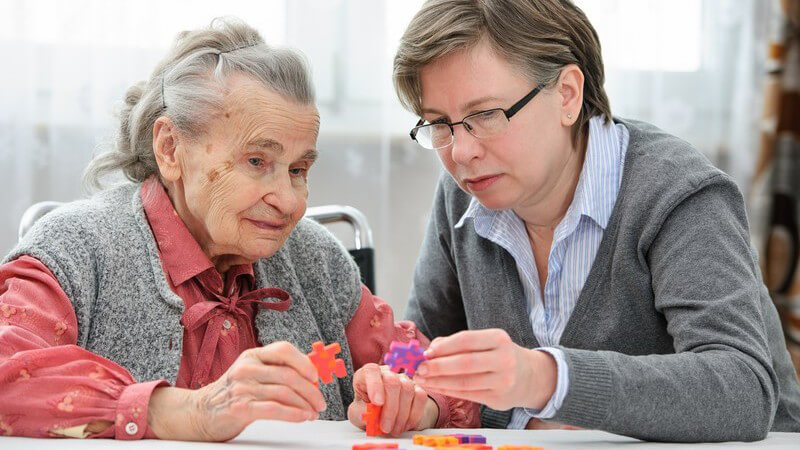 Gedächtnistraining im Altenheim - Seniorin mit Altenpflegerin oder Tochter beim Puzzeln