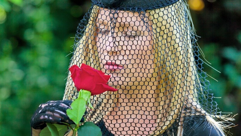 Trauer einer Witwe - schwarz gekleidete Frau mit Hut und Schleier hält rote Rose