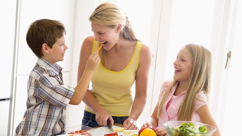 Mutter mit ihren beiden Kindern in Küche beim Gemüseschneiden