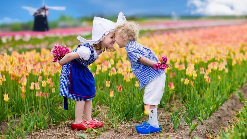 Zwei Kinder in niederländischen Trachten stehen in einem Tulpenfeld, im Hintergrund eine Windmühle