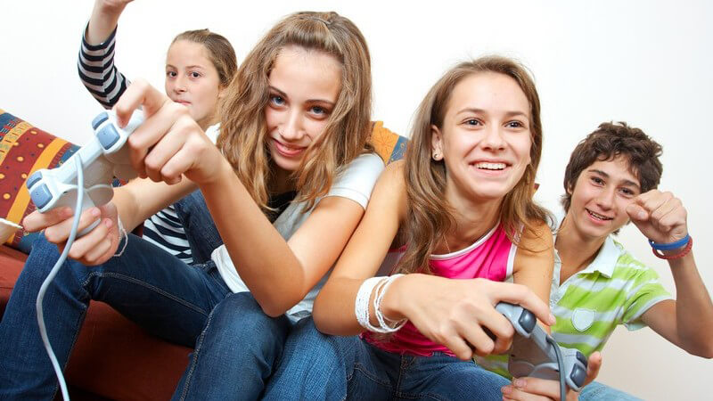 Vier Jugendliche sitzen auf Couch vor TV und spielen mit Spielkonsole
