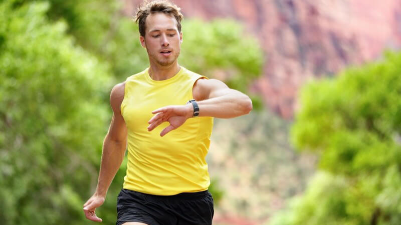 Jogger in gelben Shirt beobachtet während des Laufens seine Herzfrequenz auf der Smartwatch