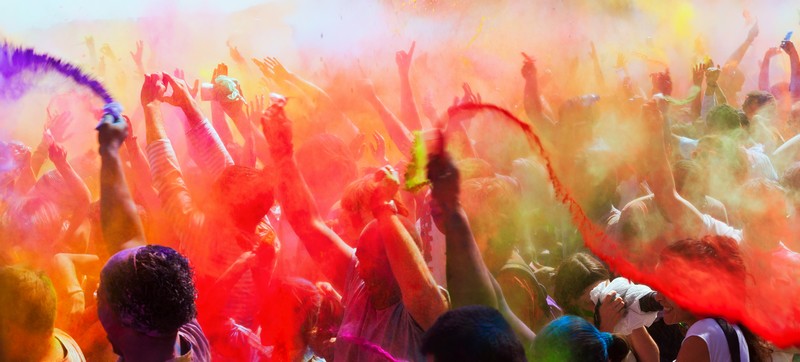 Holi Festival: Menschenmenge wirft mit bunten Farben um sich und tanzt