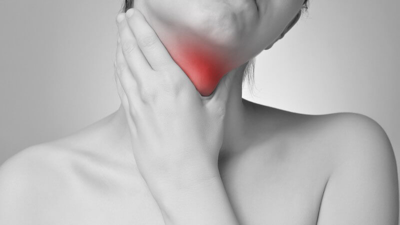 Schwarz-weiß-Foto einer jungen Frau, die sich vor Schmerzen an den Hals fasst, der Hals/Rachen rot hervorgehoben
