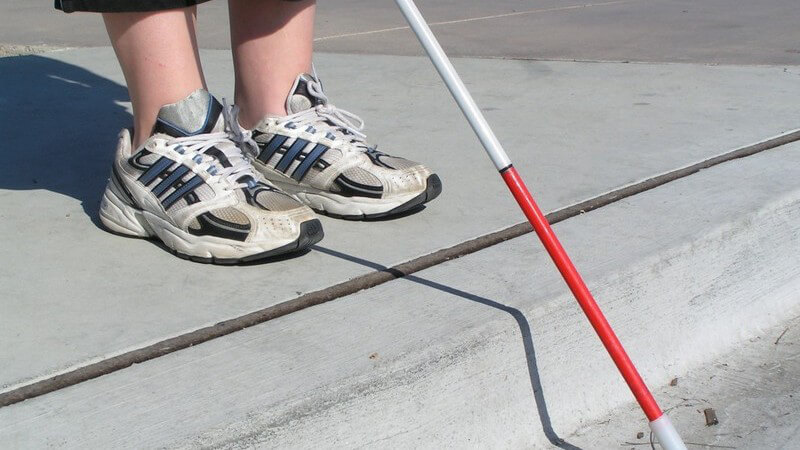 Füße eines Blinden mit Blindenstock an Straße