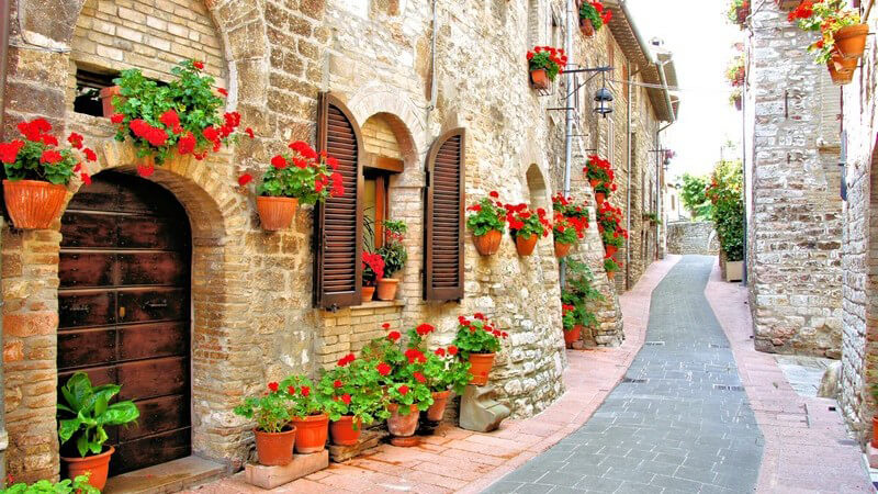 Italien: Gasse eines italienischen Dorfes mit roten Blumen an Häusern mit Fensterläden
