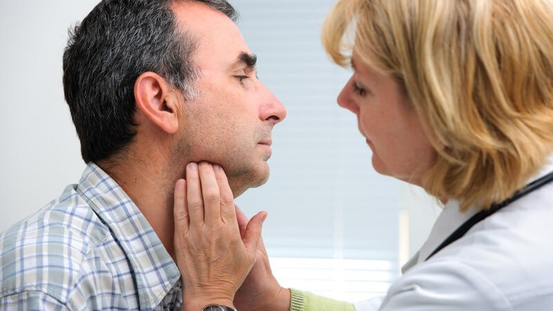Ärztin untersucht die Schilddrüse eines Mannes durch Abtasten am Hals