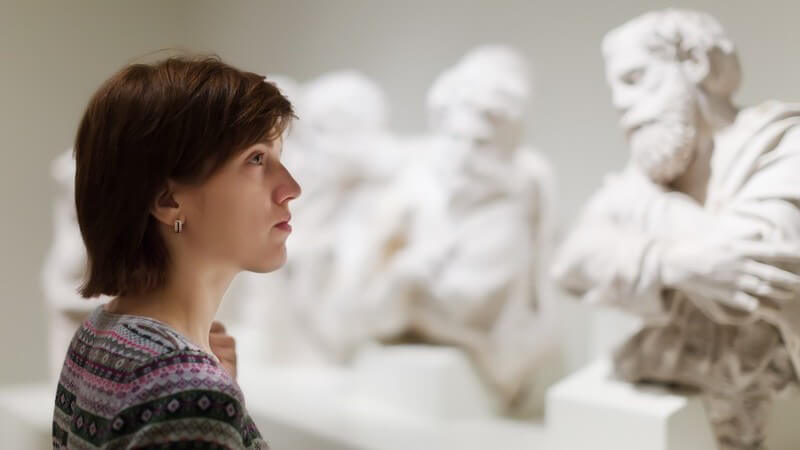 Frau betrachtet in einem Museum weiße, antike Skulpturen/Statuen