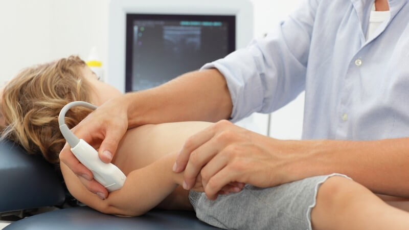 Arzt untersucht den Ellenbogen eines Kindes per Ultraschallgerät