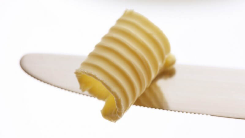 Nahaufnahme einer Butterlocke auf Messerspitze, weißer Hintergrund, Margarine