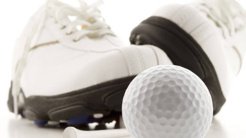 Nahaufnahme weiße Golfschuhe hinter Golfball auf weißem Hintergrund