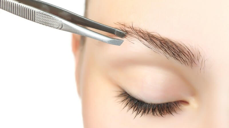 Frau zupft sich die Augenbrauen über dem rechten Auge mit einer Pinzette (Nahaufnahme)