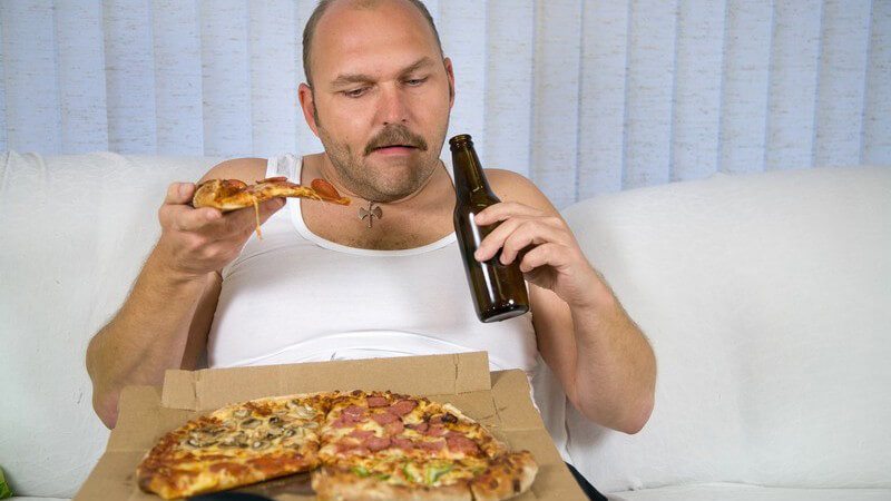 Mann im Unterhemd mit Bierflasche und Pizza auf Couch