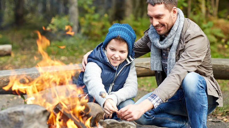 Vater und Sohn hocken zusammen an einem Lagerfeuer vor einem Wald