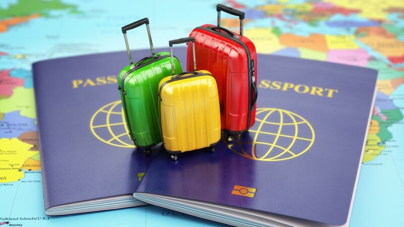 Zwei lila Reisepässe und farbige Miniaturkoffer auf einer Weltkarte