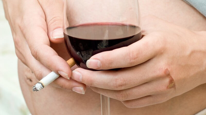 Nahaufnahme Babybauch, Schwangere hält Glas Wein und Zigarette in der Hand