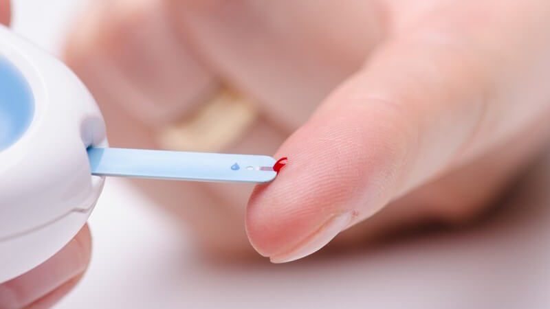 Blutzuckermessgerät nimmt Blut vom Zeigefinger zur Blutzuckermessung