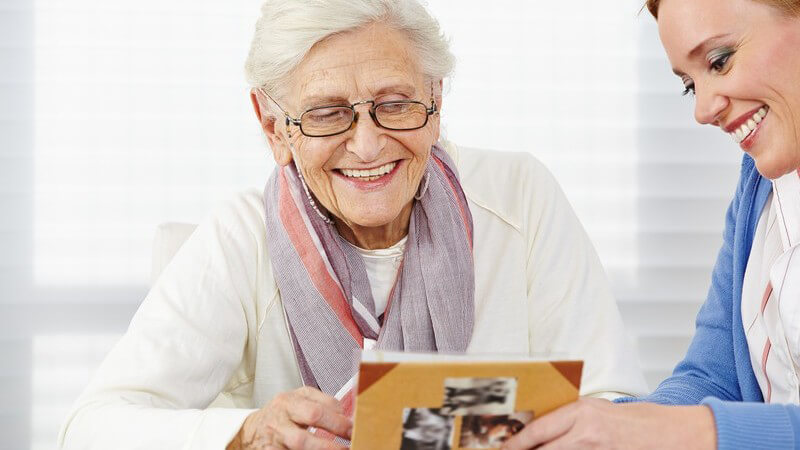 Lächelnde Seniorin sieht sich mit ihrer Tochter ein altes Fotoalbum an