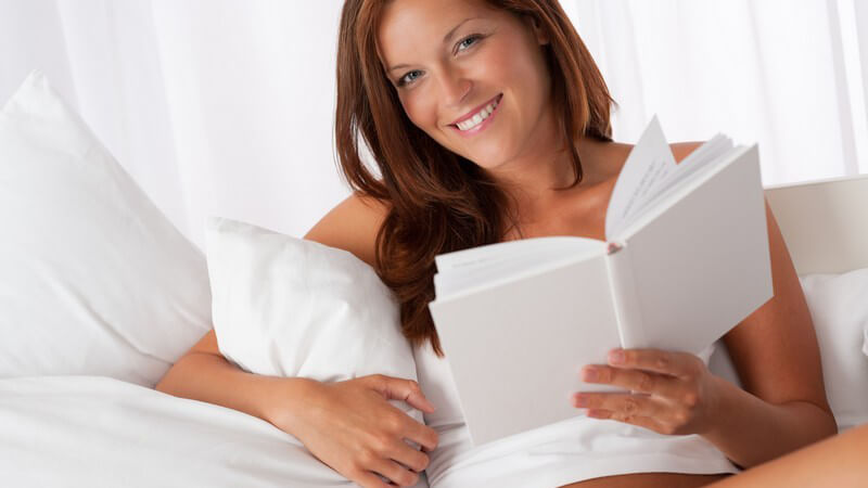 Junge Frau in weißer Unterwäsche liegt mit weißem Buch im Bett