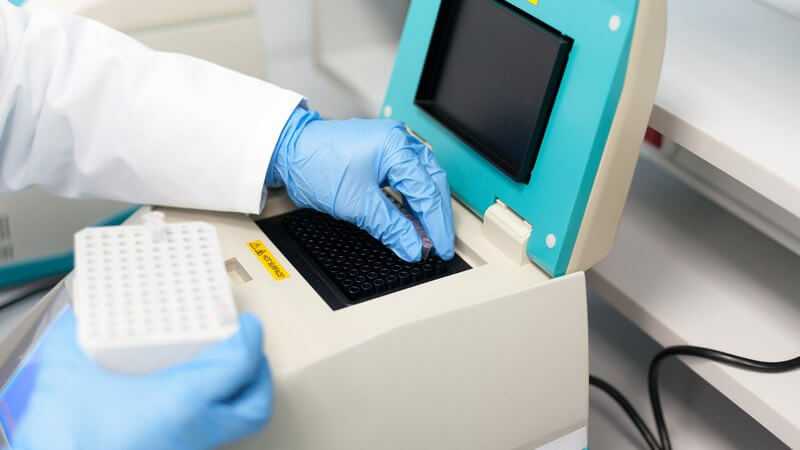Laborant füllt Röhrchen mit DNA-Proben in ein Analysegerät