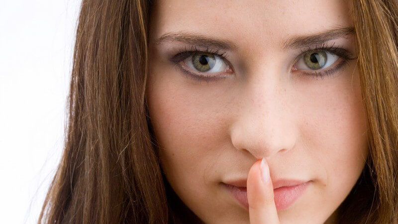 Gesichtsportrait, junge Frau hält Zeigefinger vor geschlossenen Mund